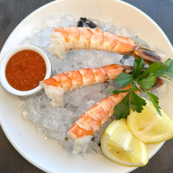 Three large shrimp on a bed of ice with cocktail sauce, lemon wedges, and parsley.