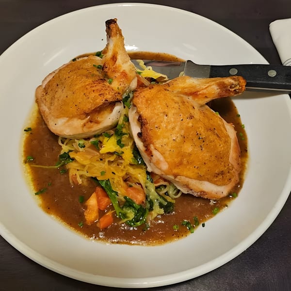 Two pieces of roasted chicken with crispy skin, served over vegetables and gravy on a white plate.