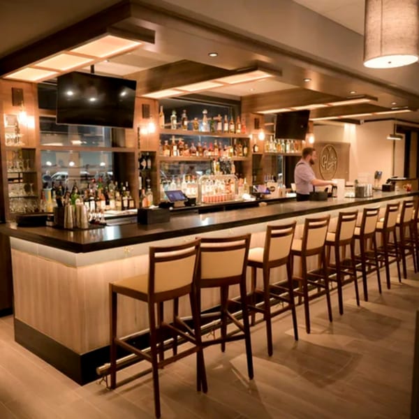 A well-lit bar at Hilltop Kitchen & Bar with a bartender, bottles, and empty bar stools.