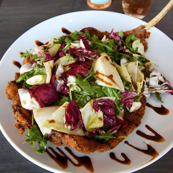 Crispy fried chicken schnitzel topped with a fresh salad of mixed greens, radicchio, and cheese.