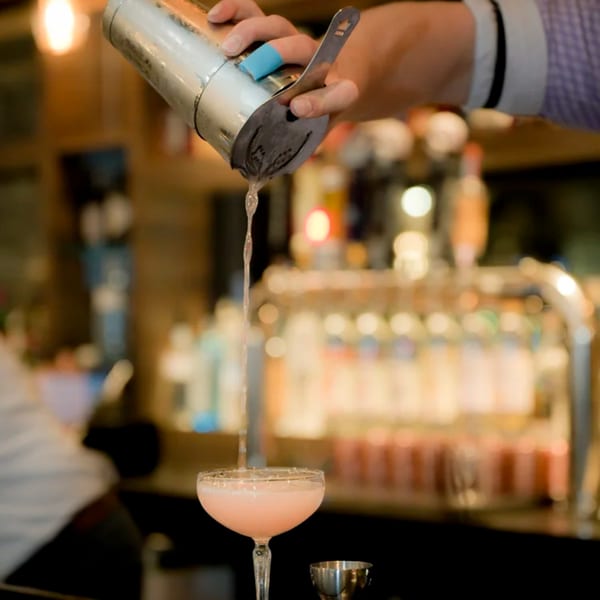 A bartender pours a pink cocktail from a shaker into a coupe glass at Hilltop Kitchen & Bar.