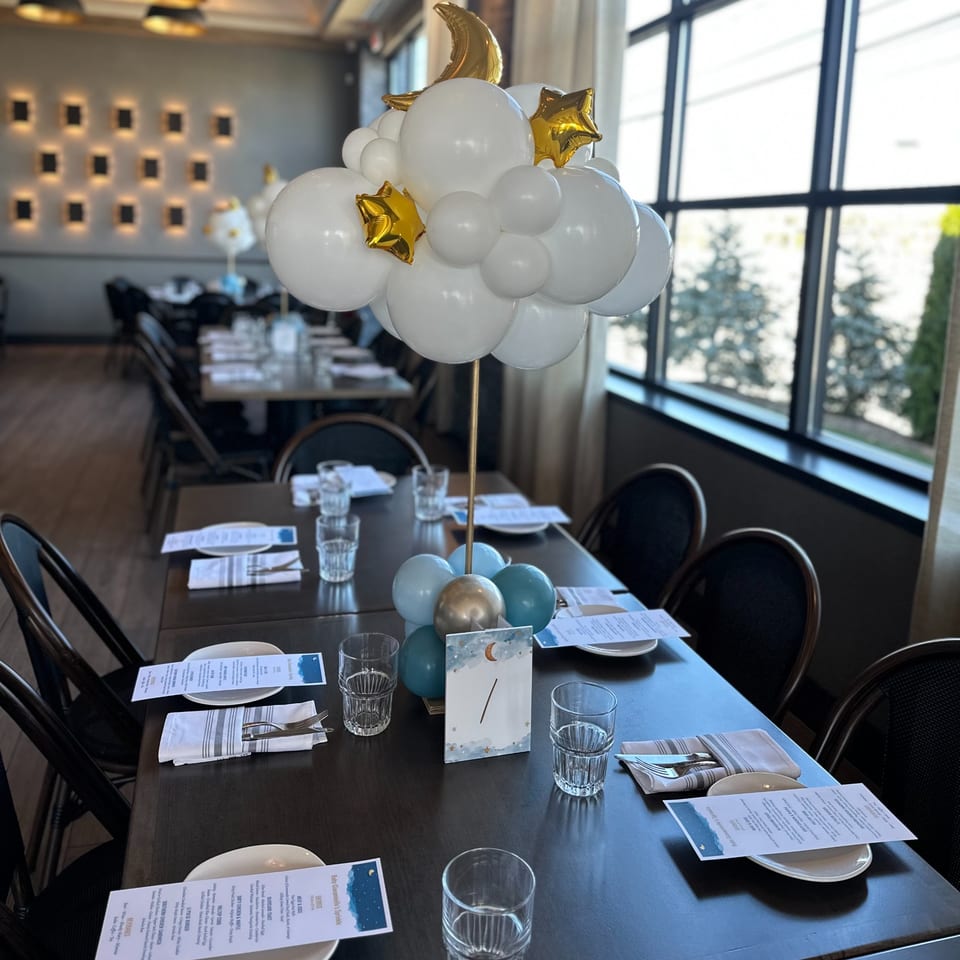 A restaurant table set with menus and a white and gold balloon centerpiece, with other tables in the background.