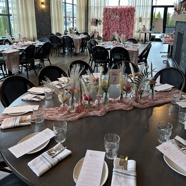 A restaurant dining room set up for a baby shower with decorated tables and a pink floral wall.