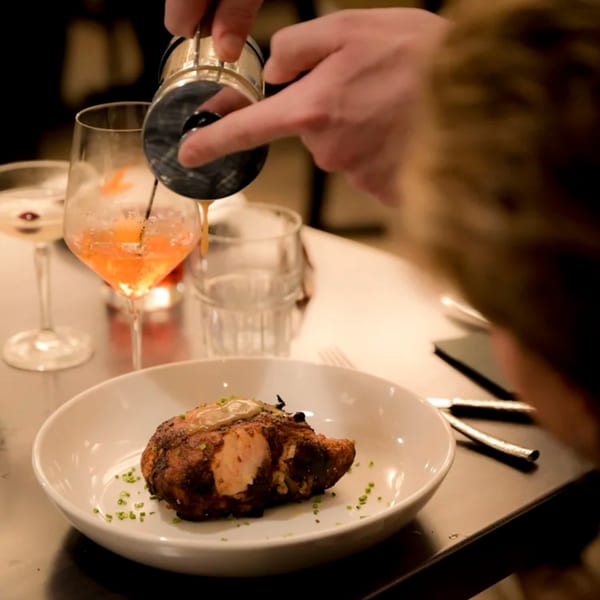 A chef pours a drink into a glass next to a plate of roasted chicken at Hilltop Kitchen & Bar.