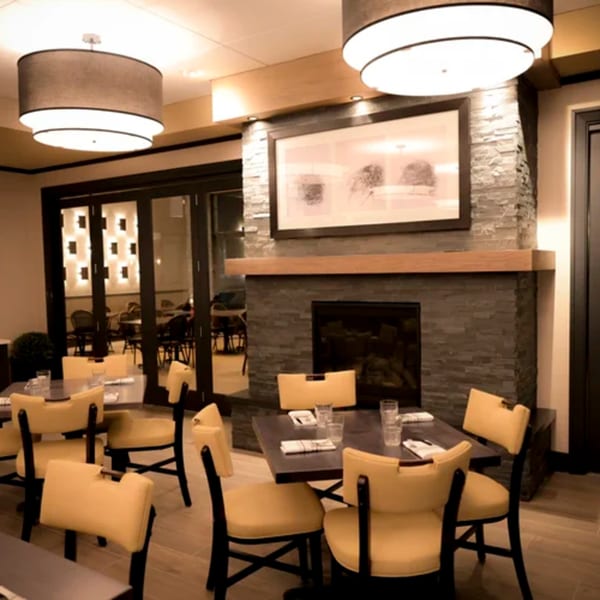 Dining room at Hilltop Kitchen & Bar with yellow chairs, dark tables, and a stone fireplace.