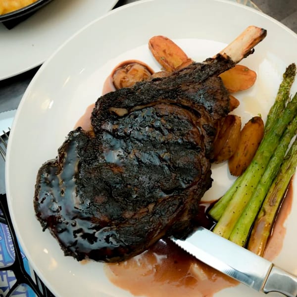 A large, dark steak with bone, roasted potatoes, and asparagus on a white plate.