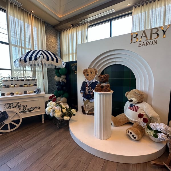 A baby shower setup with a cupcake cart, teddy bears, balloons, and a "Baby Baron" sign.