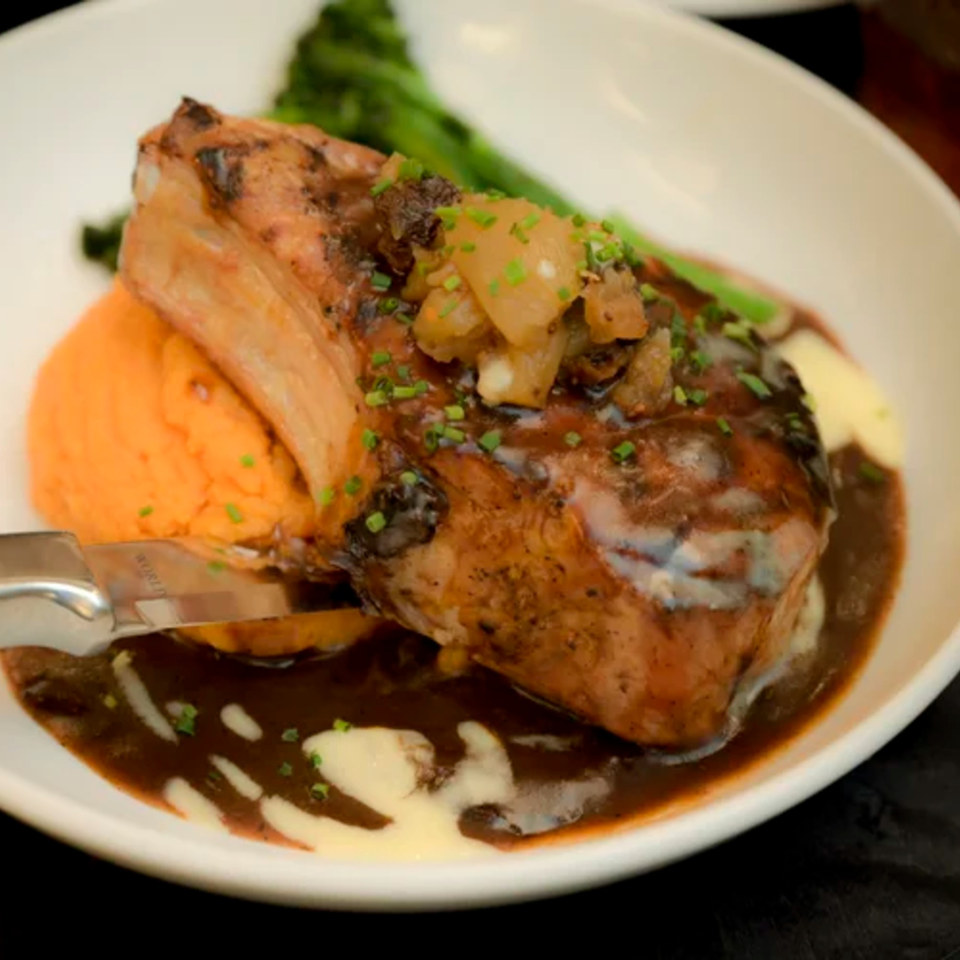 Grilled pork chop with apple chutney, sweet potato mash, gravy, and broccolini on a white plate.