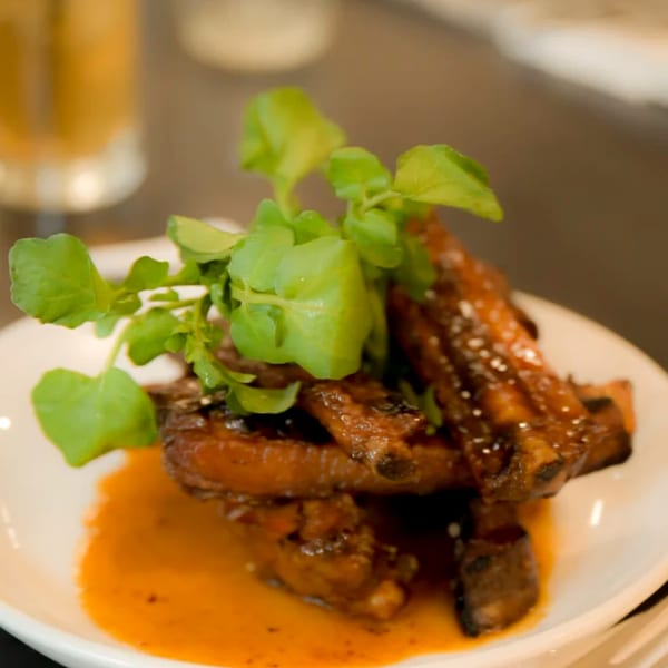 Glazed ribs with fresh greens on a white plate, served with a rich orange sauce.