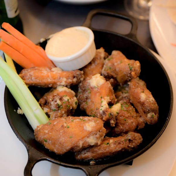 Crispy chicken wings with a creamy dip, carrot sticks, and celery in a cast iron pan.