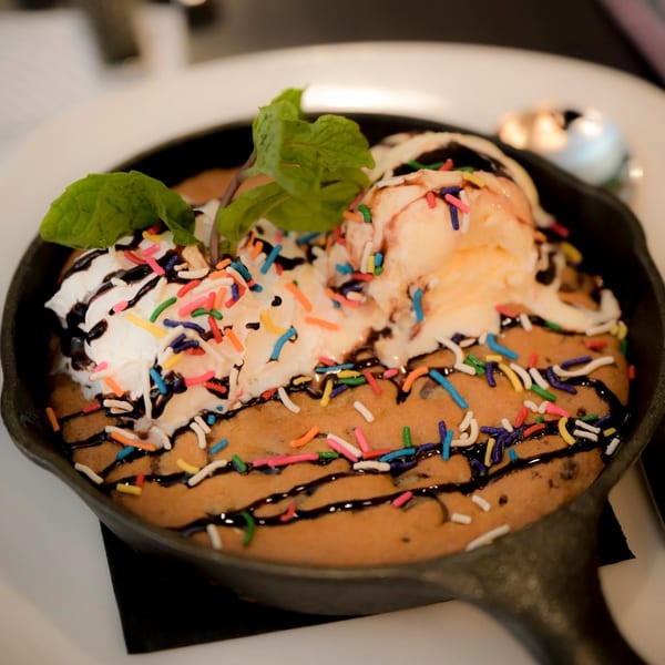 Skillet cookie with vanilla ice cream, whipped cream, chocolate drizzle, sprinkles, and mint garnish.